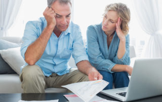 an older man and woman looking concerned going over bills and sitting with an open laptop