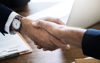 two men wearing suits shaking hands over a desk