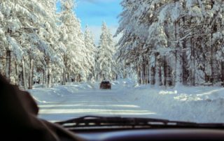 looking through the windshield at a car driving on a snow-covered road through the forest with blue skies