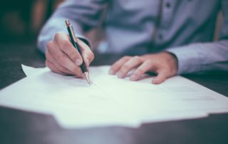 a man in a button up shirt looking over and signing documents on a desk