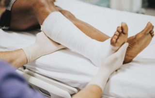 a medical worker holding a woman's bandaged and braced ankle while she sits in a hospital bed