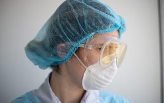 person wearing a hair covering, mask, and safety goggles looking to the side