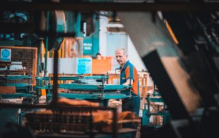 man wearing blue and orange uniform working in a factory using metal machinery