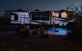 large black and white RV at dusk with people sitting outside