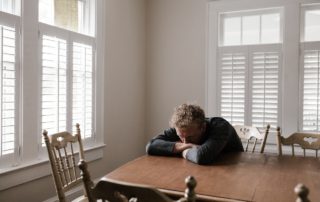 man with his head down at a dining table in well lit white dining room