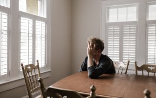 a worried man sitting at an empty kitchen table looking out of the window