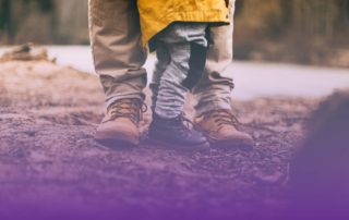 a man and toddler's lower legs standing in the dirt