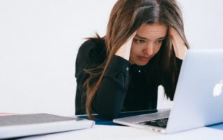 girl holding her head in her hands looking at laptop