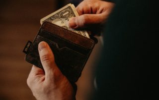 man holding dollar bills partly out of a brown wallet